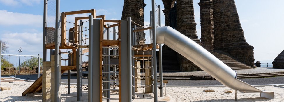 Klettergerüst mit Rutsche vor einem Denkmal