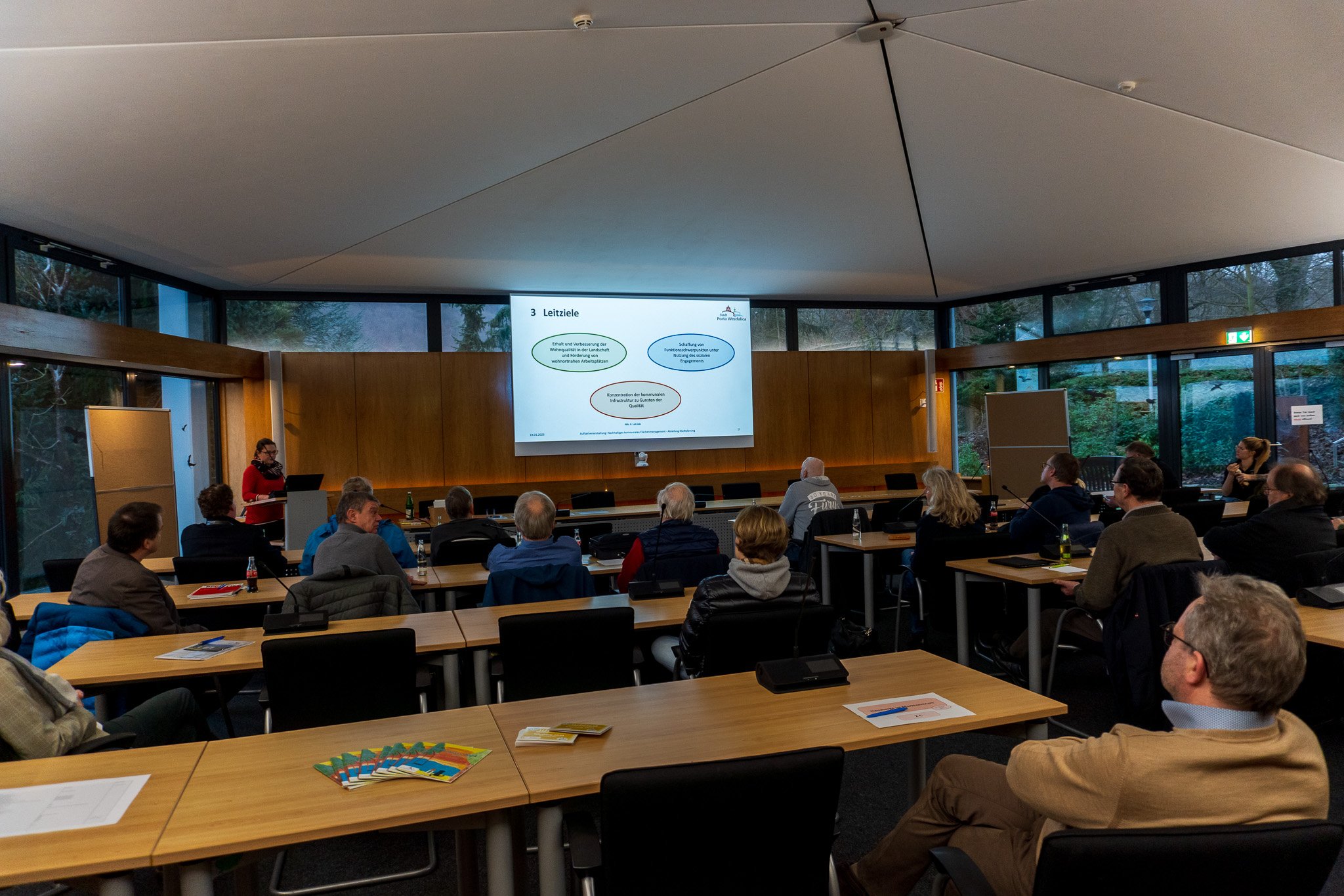 Menschen sitzen in einem Saal und schauen auf eine Leinwand