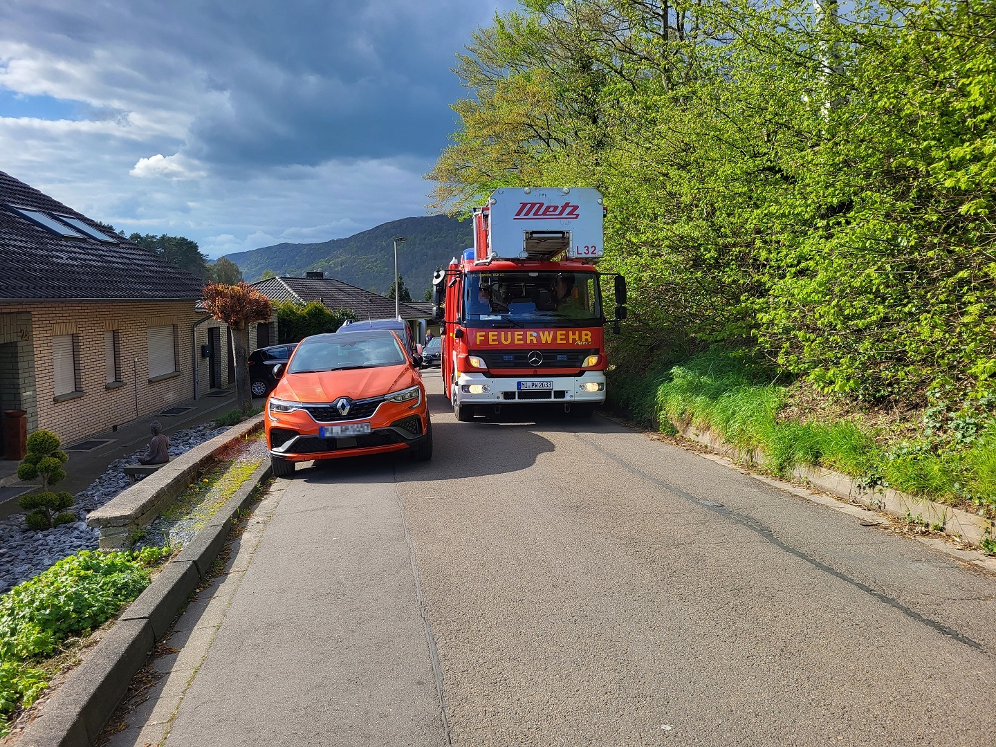 Ein Feuerwehrauto fährt auf einer engen Straße an einem parkenden Auto vorbei