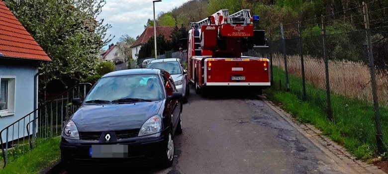 Ein Drehleiterfahrzeug fährt an zwei parkenden Autos vorbei