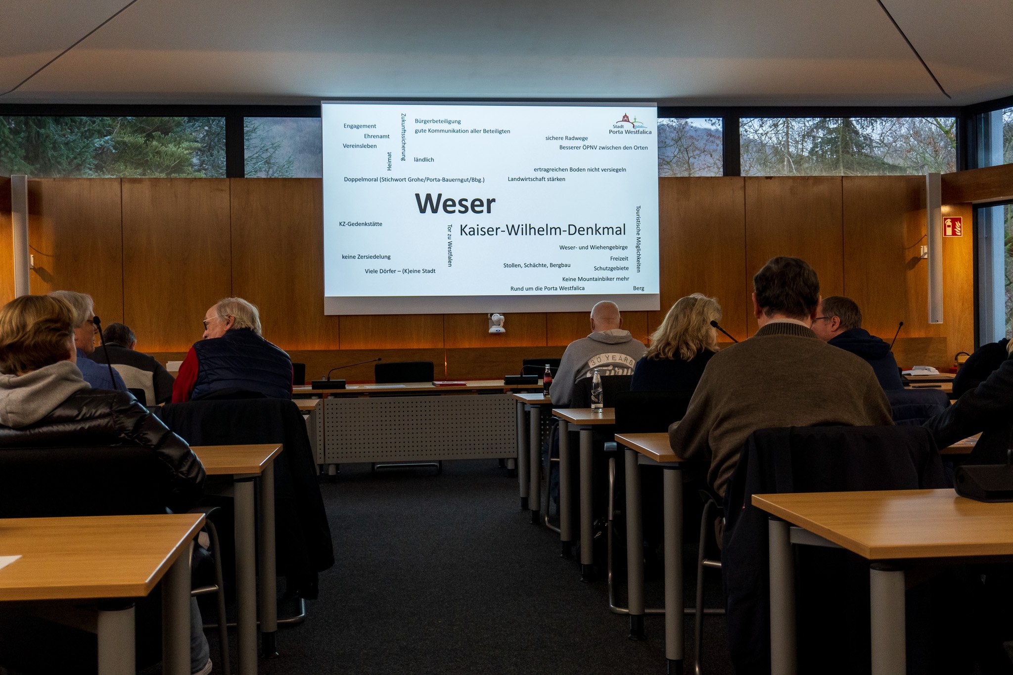 Menschen sitzen in einem Sitzungsraum vor einer Leinwand