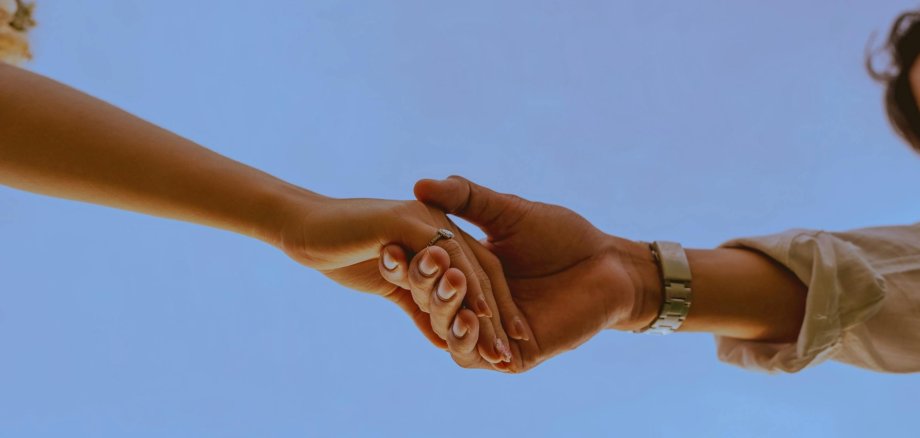 Zwei Hände, die einander halten vor blauem Hintergrund 